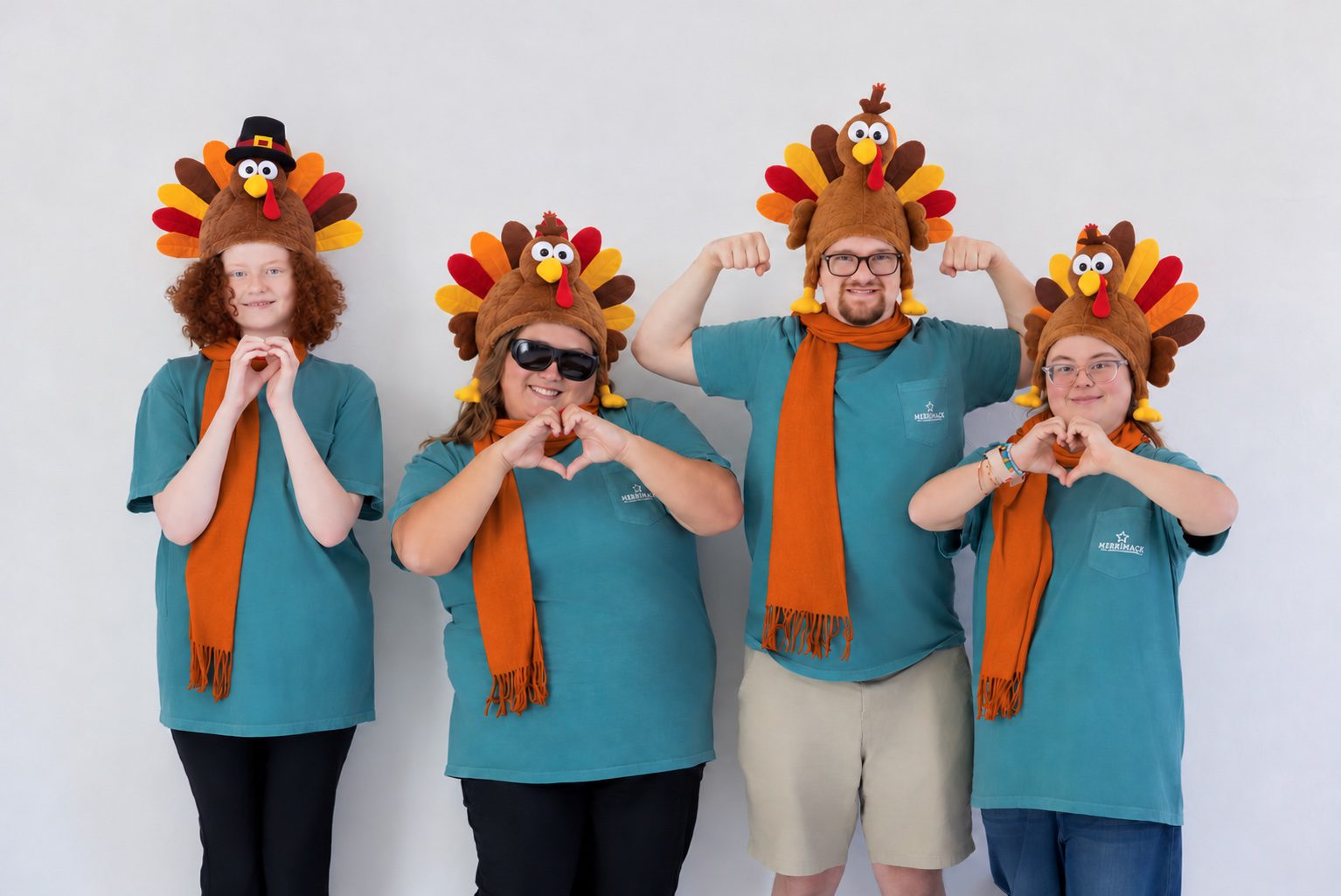 Four Merrimack Huntsville students in turkey hats and orange scarves making heart shapes with their hands